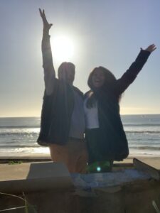 Lance and Tammy shadowed to near-silhouettes in front of the sun with their arms thrown up at the beach.